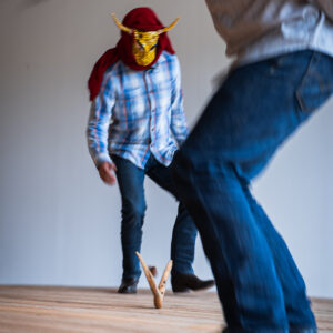 Two dancers in jeans and checkered button-ups dance around a wooden sculpture.