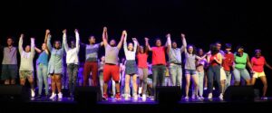 Multiple teens hold hands at the edge of the stage and raise arms up