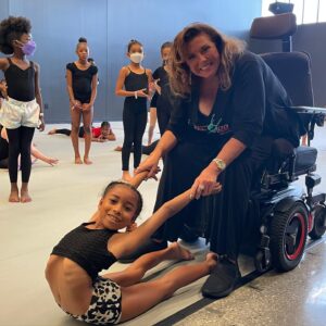 Ms. Abby stretches a young dancer's back bend while in a wheelchair.