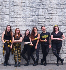 Drumatix group poses in black and yellow costumes against a grey stone wall