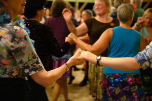 Many dancers in colorful clothing hold hands and dance together.