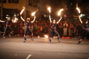 Dancers on stage have torches with flames on both hands as the audience watches