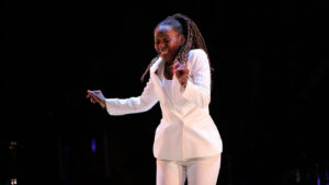 Female-presenting person dances wearing an all-white suit in a dark space.