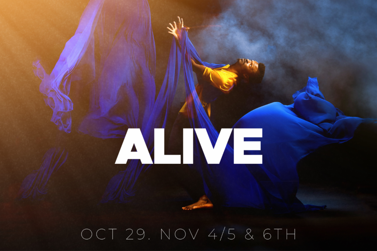 Dancer in a dark smokey space wearing golden silky shirt looks and reaches arms up holding long blue flowy fabric