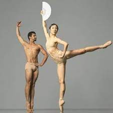 Photo of 2 Boston Ballet dancers in skin-toned briefs (and female-presenting dancer wears skin-toned sports bra as well). Male-presenting dancer is on parallel relevé with left hand on hip and right arm rounded up; female-presenting dancer is on pointe in an arabesque with left hand on hip and right arm rounded up holding on to an open white fan.