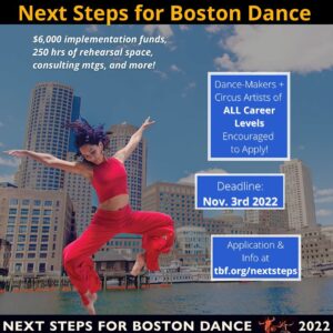 Image of dancer jumping with both legs bent and both arms up to a V position in front of the Boston seaport area.