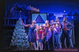 Photo of cast on stage looking up at the tip of a wand held by one of the characters up front.
