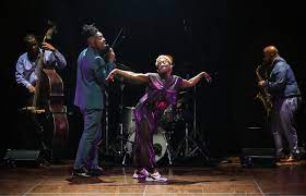 LaTasha Barnes dances with one arm and foor raised in front of her accompanying musicians