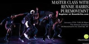 Puremovement dancers on stage wearing mostly dark baggy clothes and hopping with one arm up and one arm back.