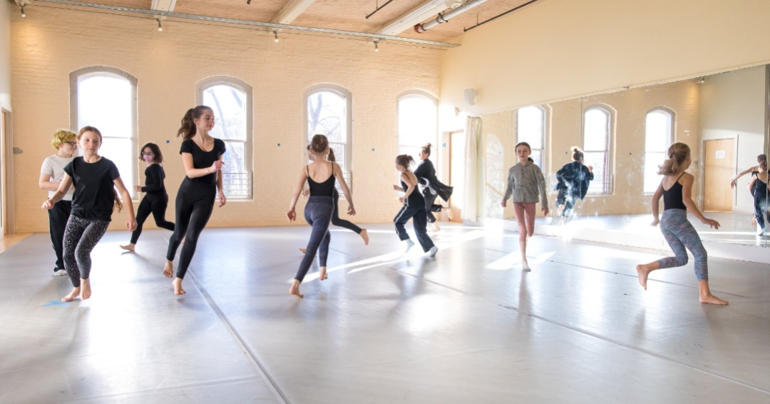 A group of dancers run inside a studio.