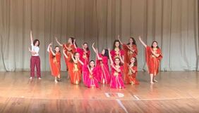 Dance group wearing orange and pink costumes posed with arms to their upper right side.