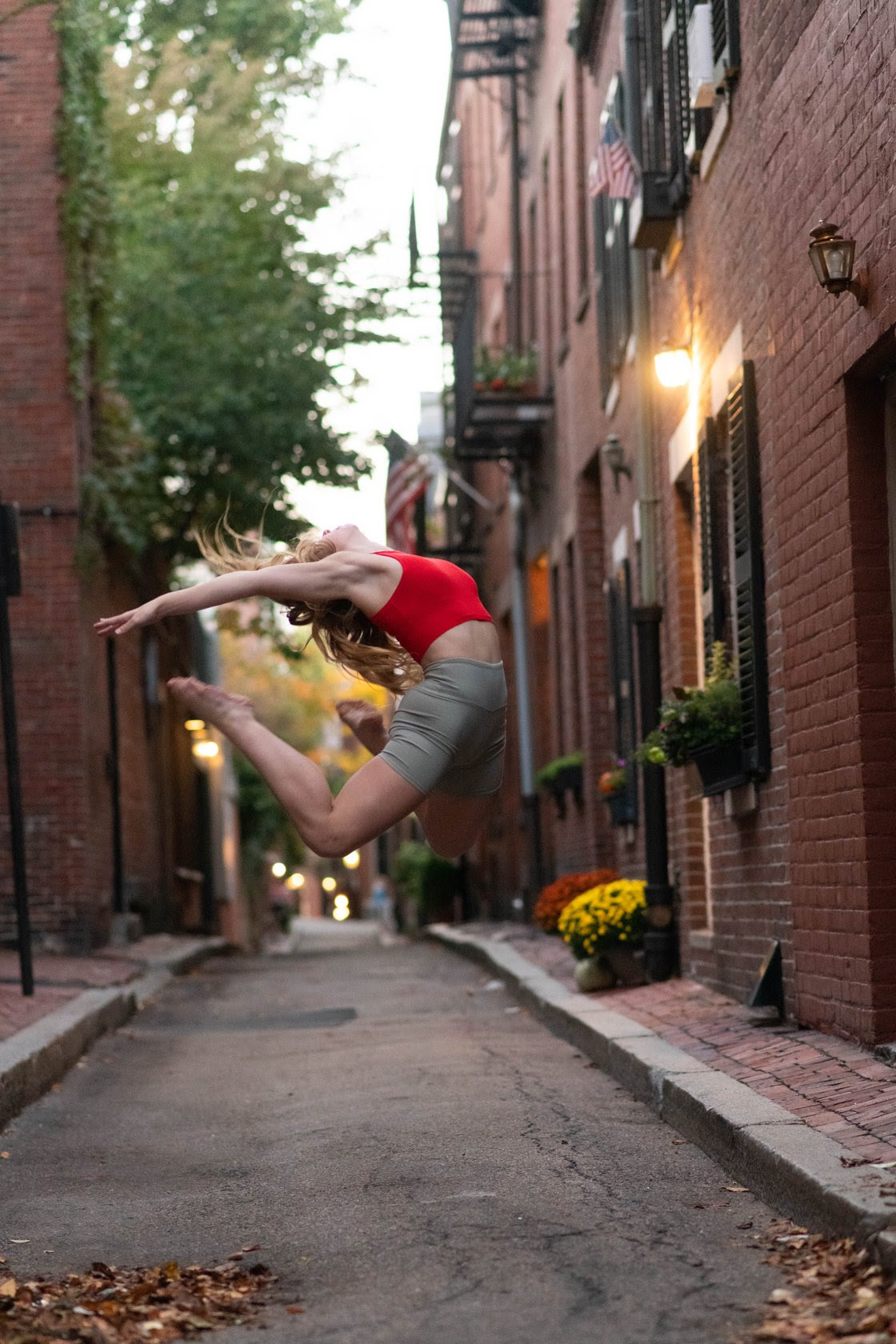 Dancer in red top and light green shorts jumps arching back, bending legs and reaching arms and head back in Beacon Hill.