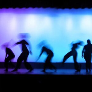 Blurred silhouette of five dancers on stage with a cold colored cyclorama as a backdrop.