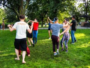 Group of people dancing in pairs on a grassy outdoor area.
