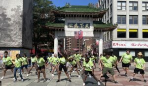 Photo of multiple teens in front of the chinatown gate dancing with bright green shirts and black shorts.