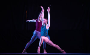 Two dancers in a lunge facing opposite directions while one holds the other's wrist.