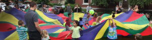Multiple kids playing with a colorful parachute and a ball outdoors.