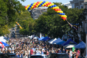 Crowd walks underneath large balloon arc in between vendor tents.
