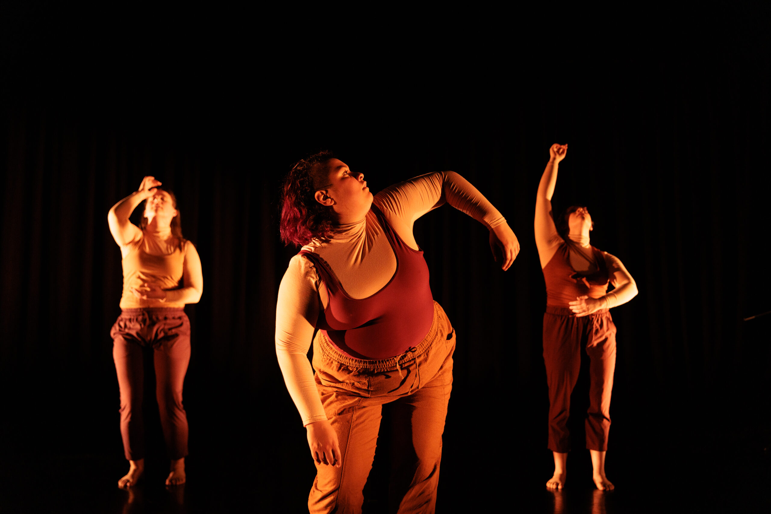 Three dancers in warm beiges and browns hold different shapes with grace