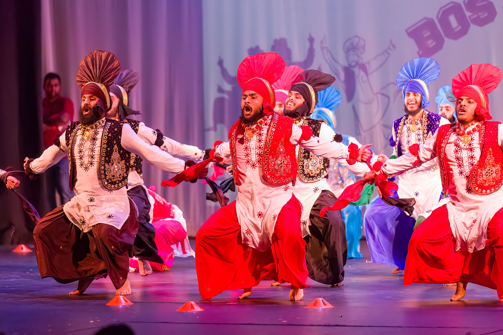 Photo of previous Bhangra Competition in which many male-presenting dancers in traditional costumes take a deep squat.