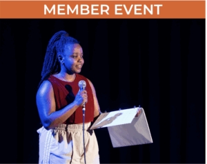 Person stands on a stage holding a microphone and open binder.