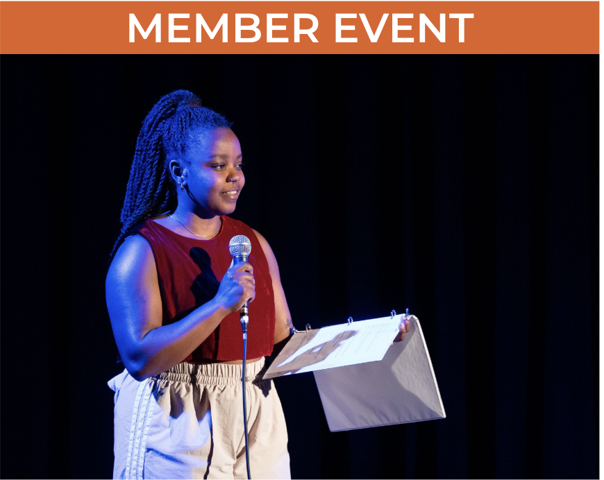 Person stands on a stage holding a microphone and open binder.