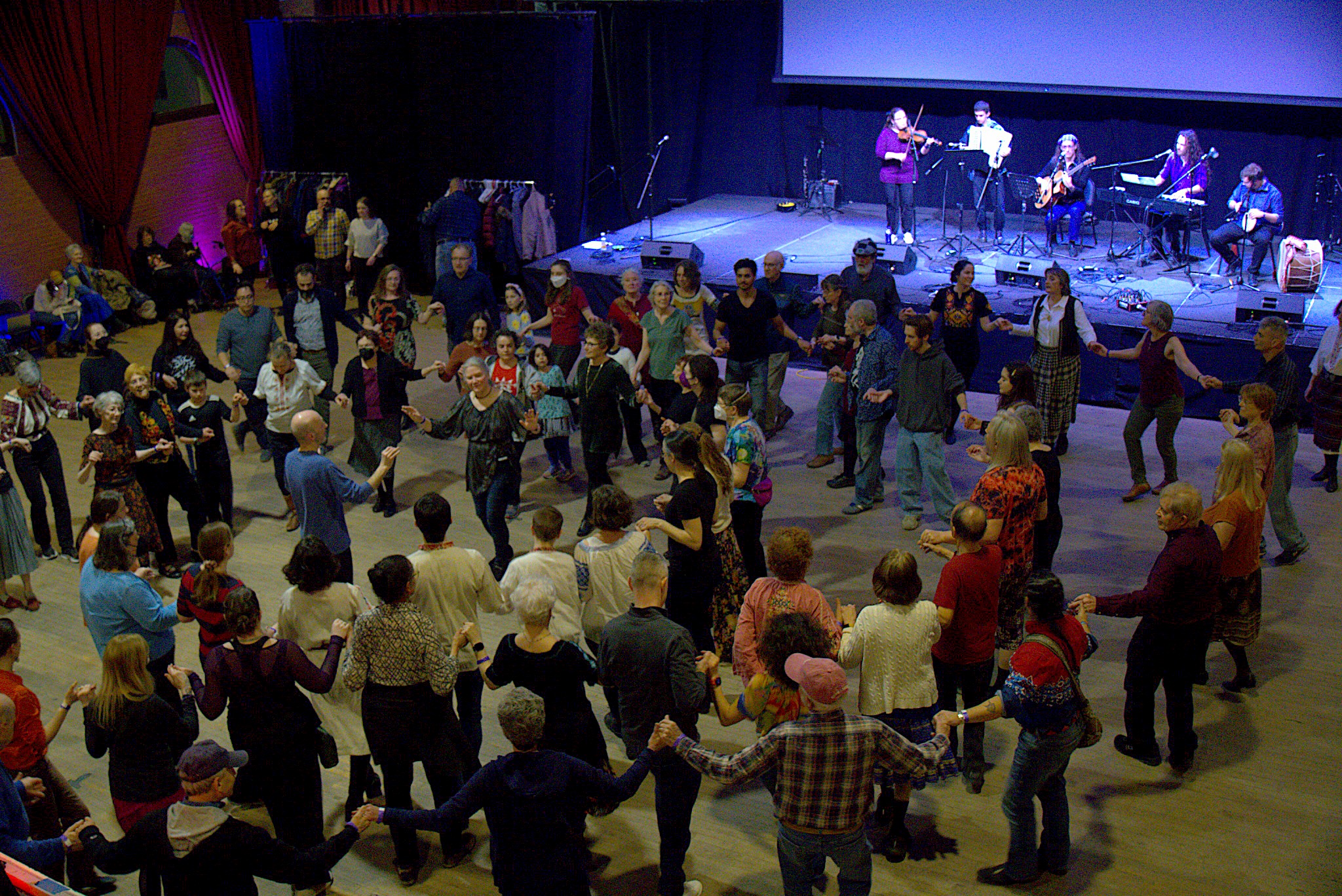 Overhead view of large group of people holding hands in circles dancing with a band in the background.